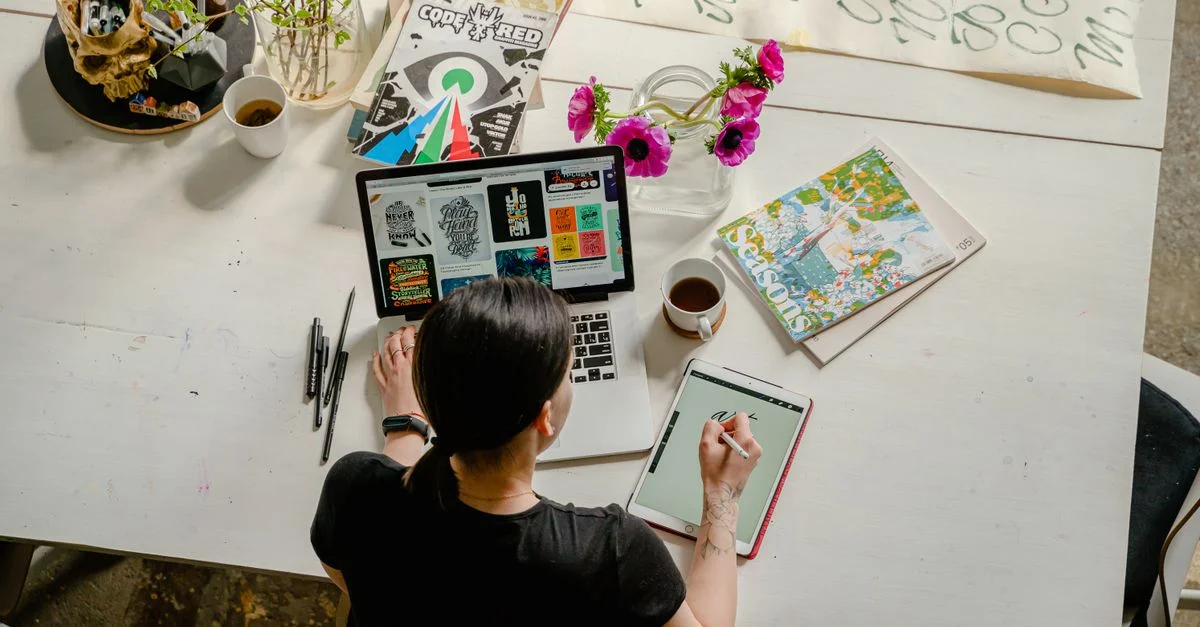 Espace de travail artistique mettant en avant la calligraphie et le design numérique sur une tablette et un ordinateur portable.