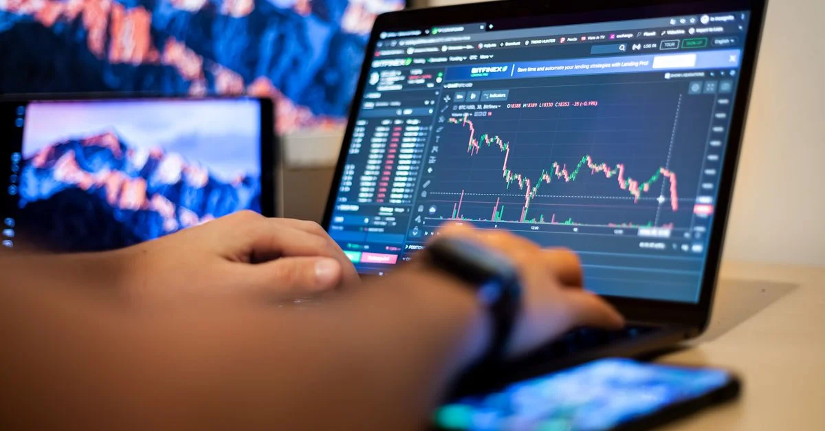 Mains tapant sur un ordinateur portable affichant des graphiques de trading financier, indiquant un travail actif de trading en ligne.