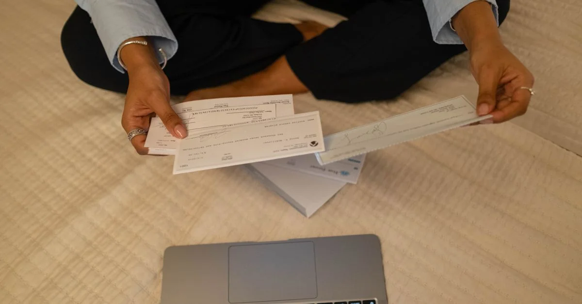 Gros plan sur des mains tenant des chèques à côté d'un ordinateur portable à l'intérieur pour des tâches financières.