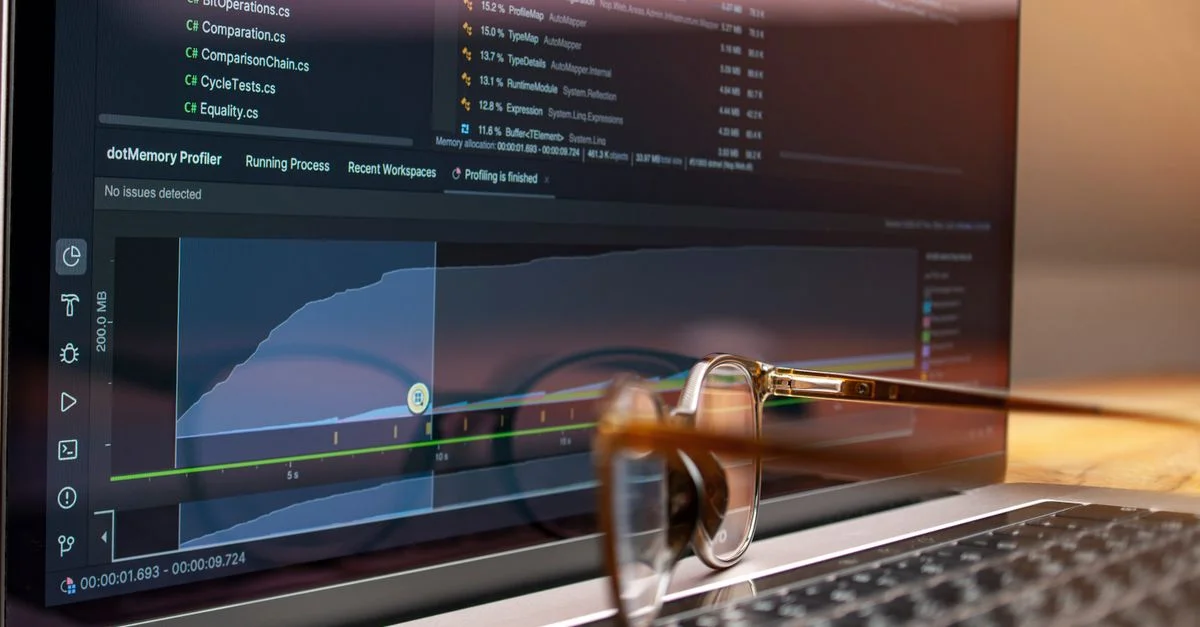 Écran d'ordinateur affichant du code et des graphiques de performance avec des lunettes reposant sur le clavier.