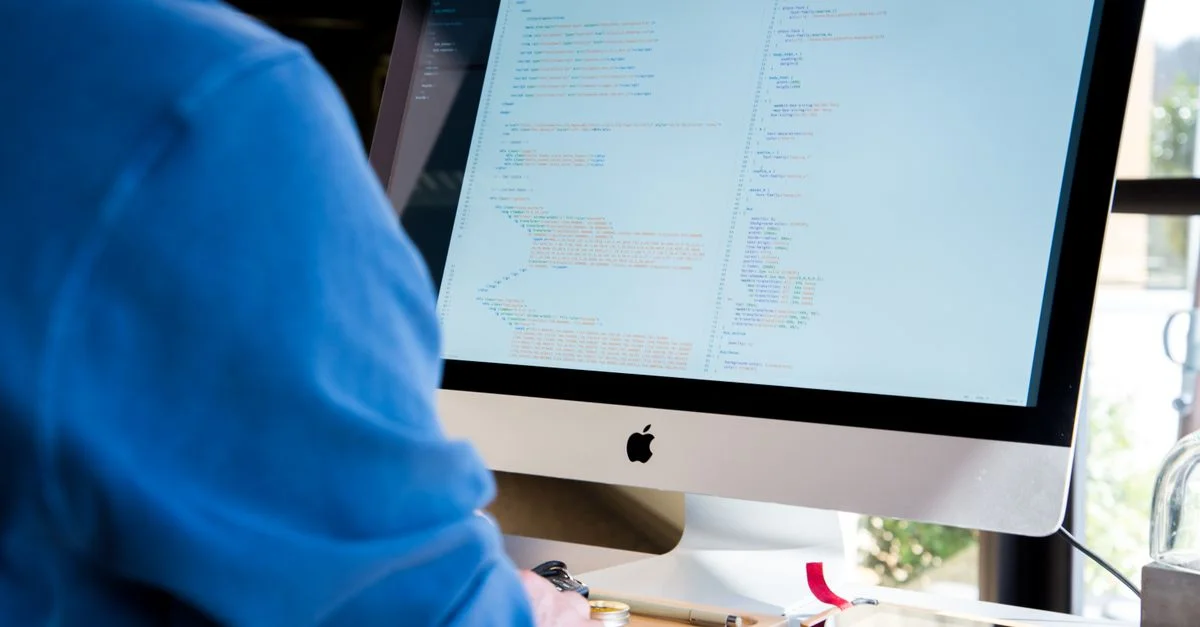 Un programmeur en chemise bleue codant sur un iMac. Parfait pour des thèmes liés à la technologie ou au travail.