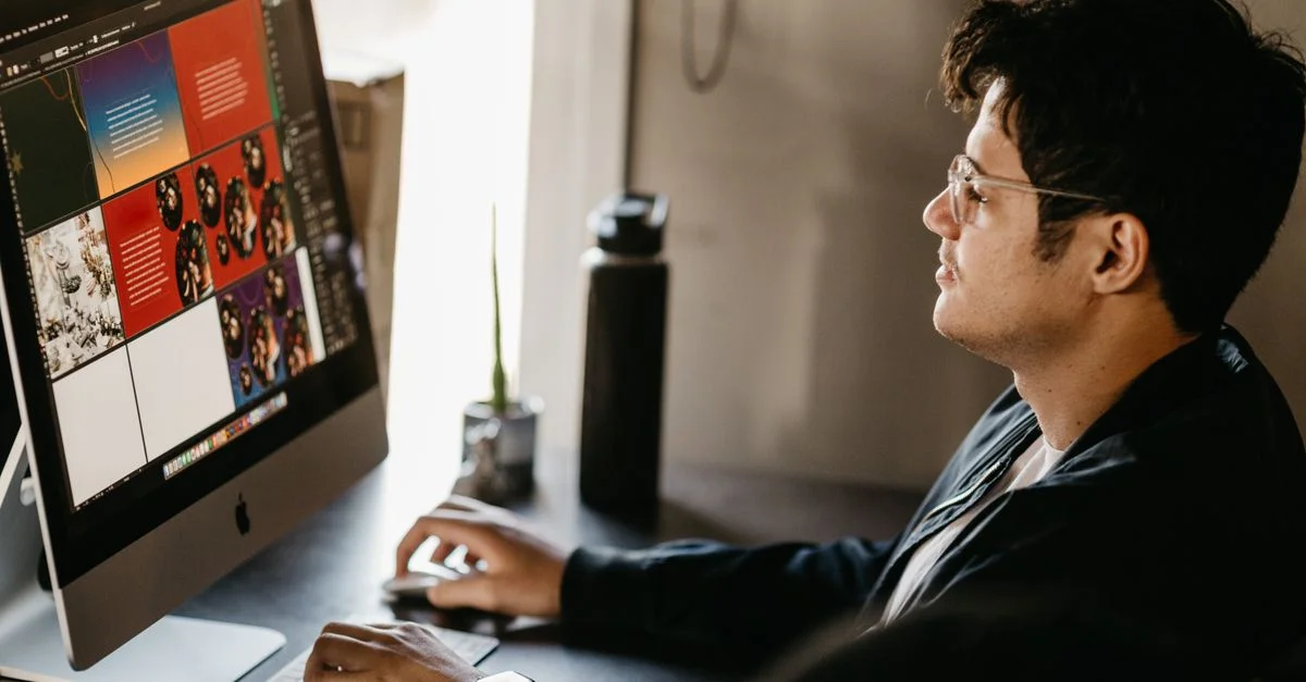 Un designer graphique concentré travaillant sur un ordinateur dans un bureau moderne avec des visuels créatifs à l'écran.