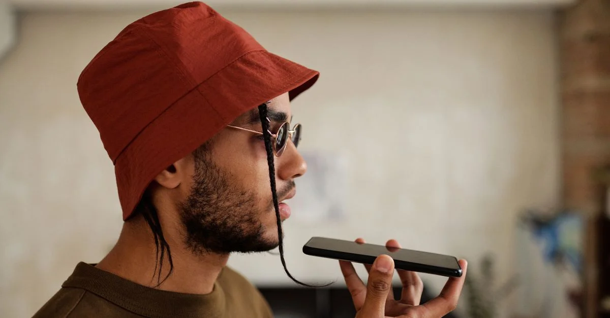 Vue de profil d'un homme portant un chapeau de seau rouge, parlant sur un smartphone à l'intérieur.