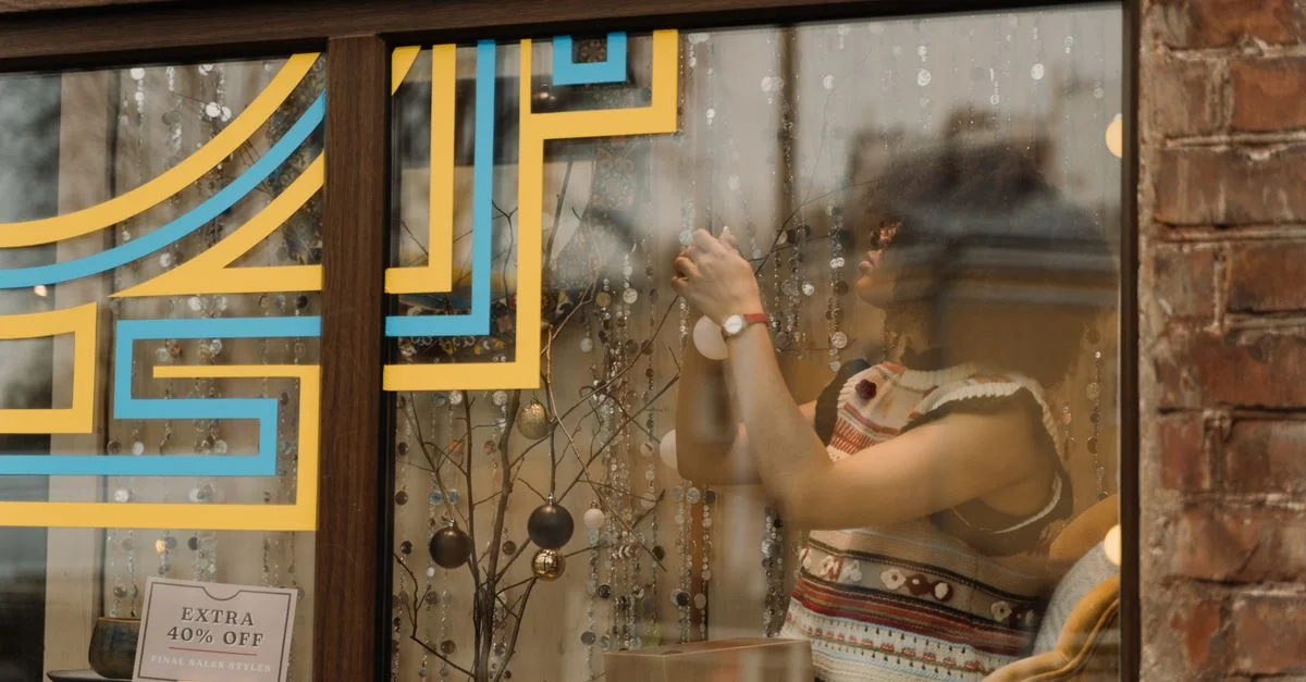 Une femme décore une vitrine de magasin avec des décorations de fête, offrant une ambiance chaleureuse et festive.
