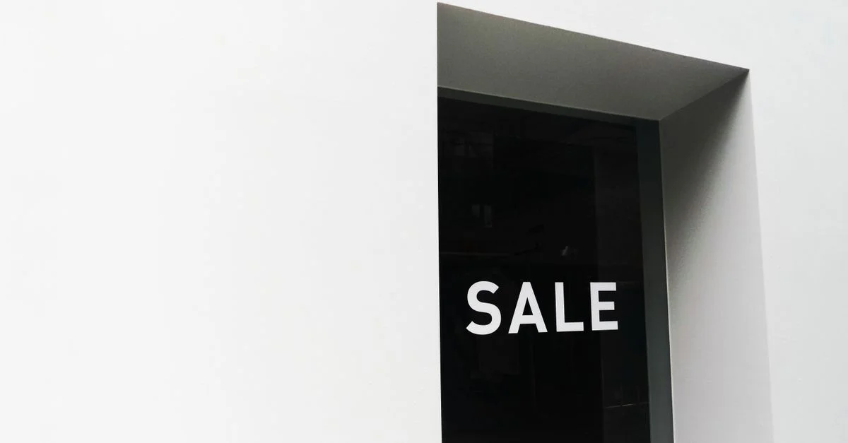 Une image minimaliste en noir et blanc d'une enseigne de solde sur une vitrine de magasin avec beaucoup d'espace négatif.